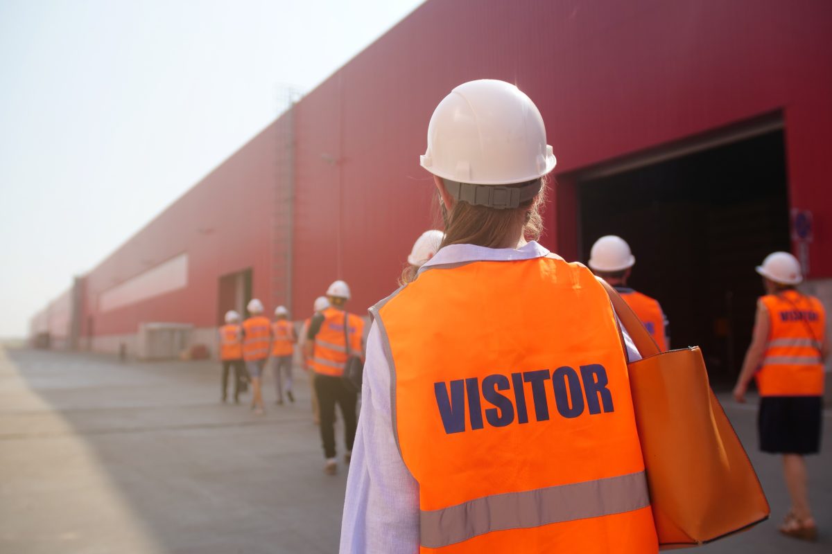 Photo of a visitor wearing PPE and a marked visitor vest on a factory tour